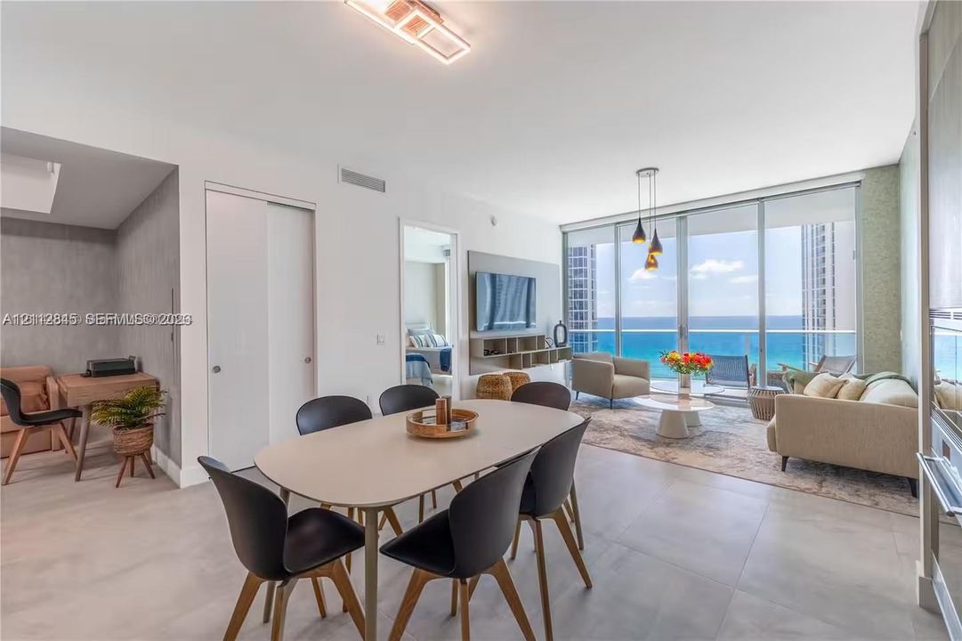Open-concept interior featuring large-format tile flooring, floor-to-ceiling glass walls, and a balcony with an ocean backdrop