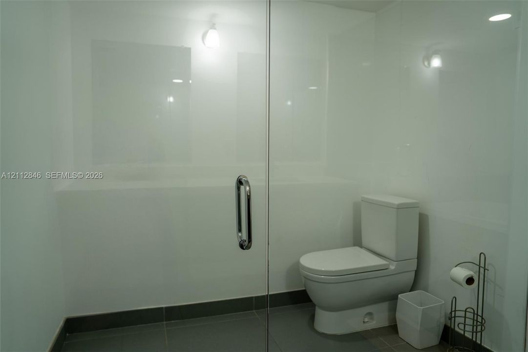 Glass-enclosed shower with white panel wall surrounds, chrome handle hardware, and large-format tile flooring