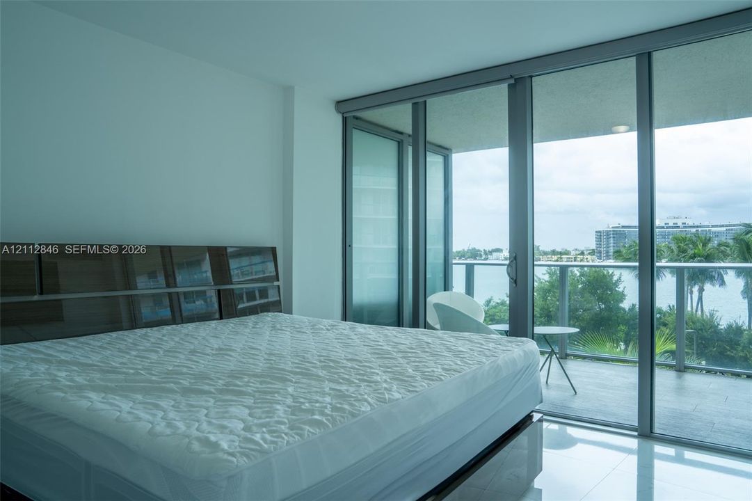 Floor-to-ceiling glass sliding doors with metallic framing, large-format tile flooring, and a private balcony featuring a glass panel railing