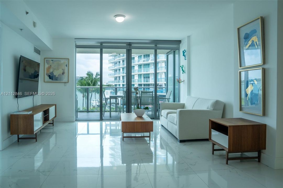 Large-format polished stone flooring, floor-to-ceiling glass sliding doors, and a private balcony with glass railing