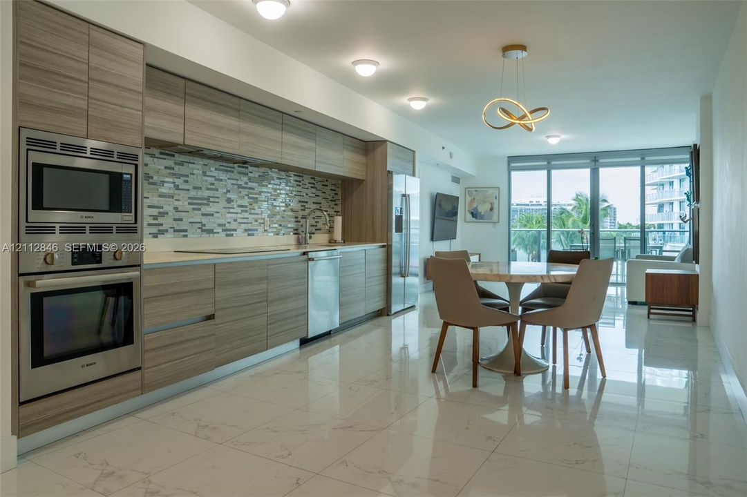 Contemporary kitchen featuring wood-finish cabinetry, stainless steel built-in oven and microwave, mosaic tile backsplash, and polished stone-finish floor tiling