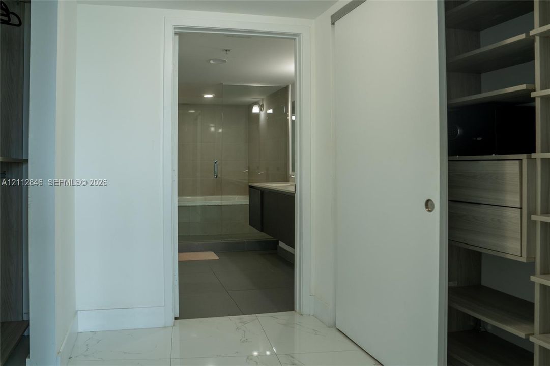 Walk-in closet with built-in wood-finish shelving and drawer storage, featuring large-format tile flooring and a sliding door