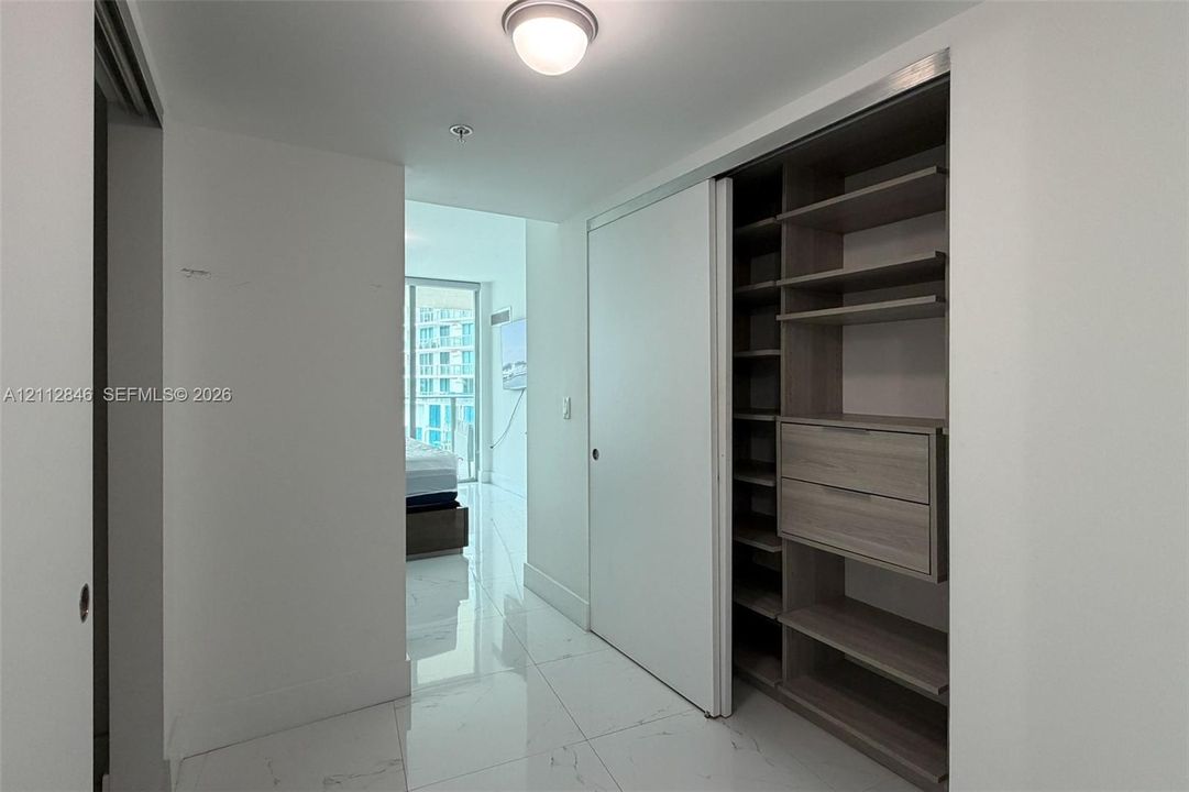 Custom closet system with integrated shelving and drawers, sliding white doors, polished stone-finish flooring, and recessed ceiling lighting