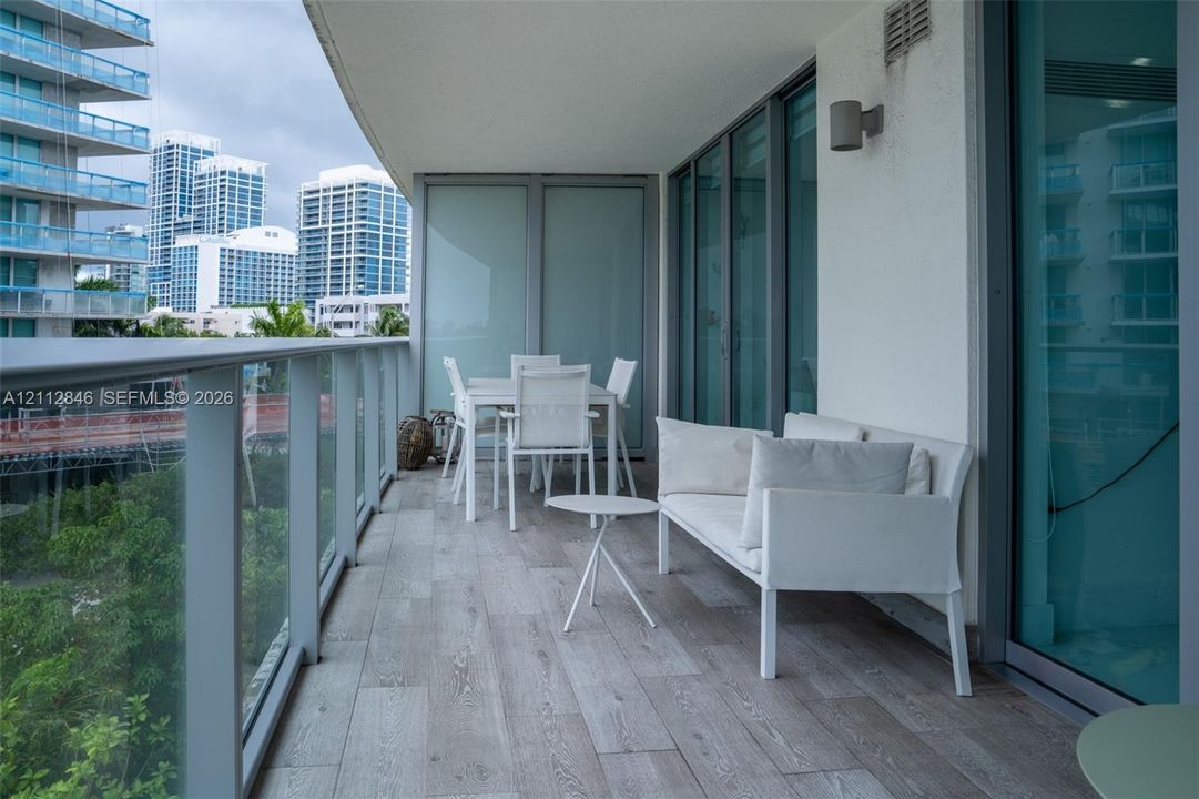 Covered balcony featuring wood-finish tile flooring, glass panel railings, and full-height sliding glass doors with brushed metal frames