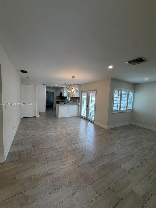 Open-concept interior featuring wood-finish tile flooring, recessed lighting, white shaker-style cabinetry, shutter window treatments, and double glass-pane doors