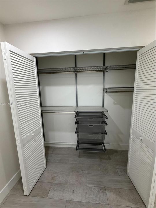 Storage area featuring white louvered doors, modular metal shelving, a built-in tiered wire drawer system, and wood-finish flooring