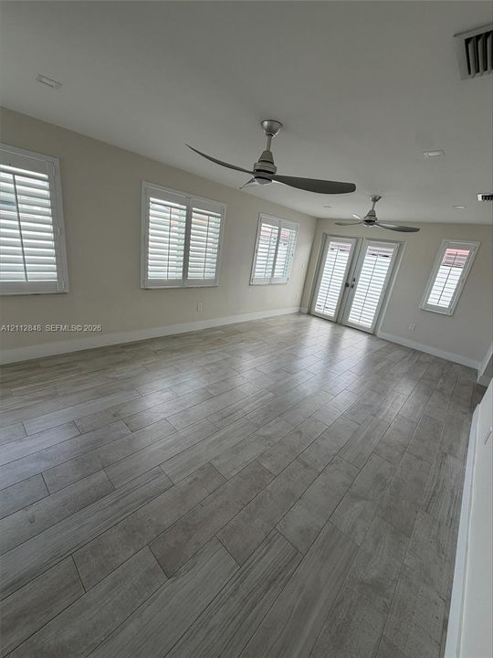 Wood-finish tile flooring, recessed lighting, dual modern ceiling fans, plantation shutters, and glass-paneled double doors