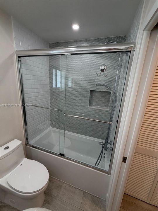 Bathtub featuring a glass sliding door, white subway tile surround, recessed wall niche, and chrome handheld shower fixture