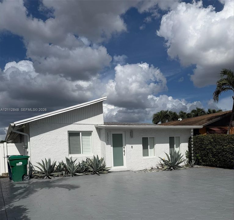 Single-story residence featuring a distinctive shed roofline, stucco exterior, paved driveway, and drought-tolerant landscaping