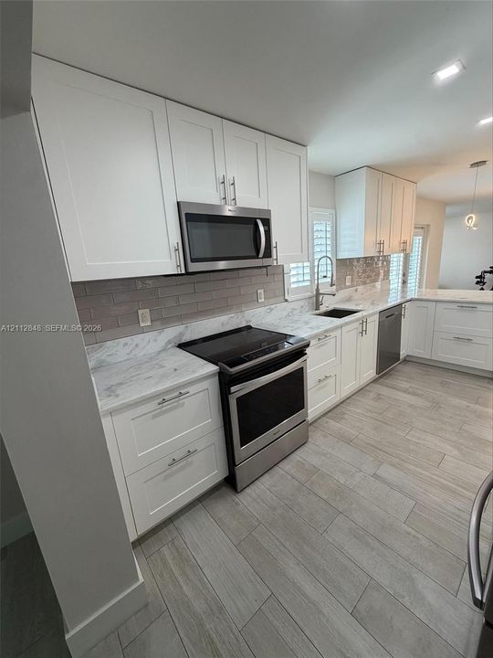 Kitchen featuring white shaker-style cabinetry, stone-finish countertops, subway tile backsplash, stainless steel appliances, and wood-finish flooring