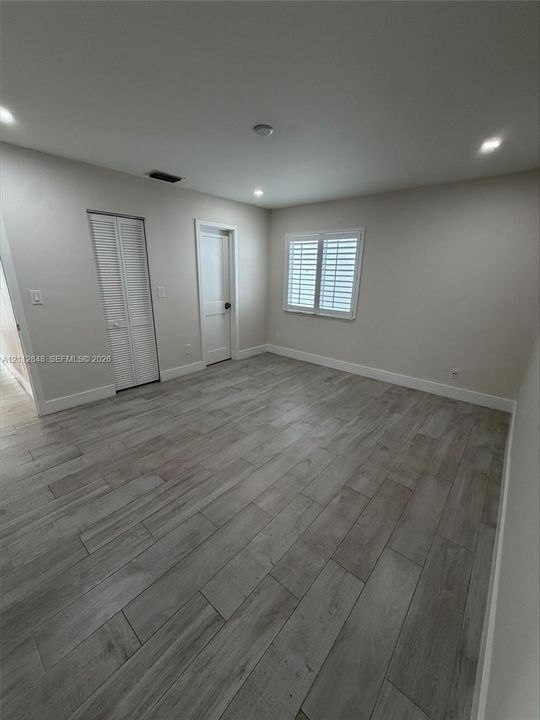 Neutral-toned interior featuring wood-finish flooring, recessed lighting, louvered closet doors, and a window equipped with plantation shutters