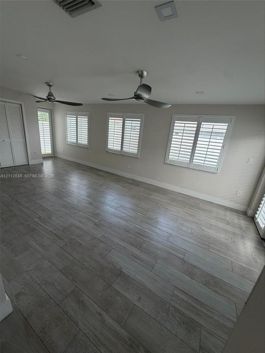 Wood-finish tile flooring, multiple windows with plantation shutters, recessed lighting, and dual ceiling fans