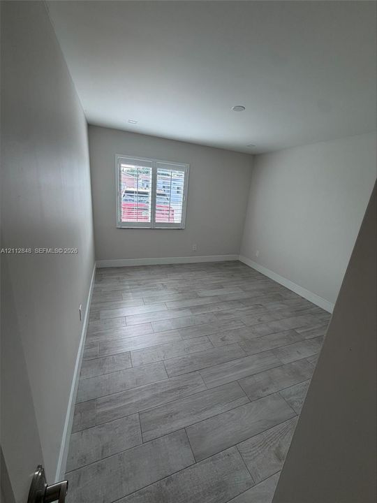 Neutral-toned interior space featuring wood-finish flooring, recessed lighting, and a single window with plantation shutters