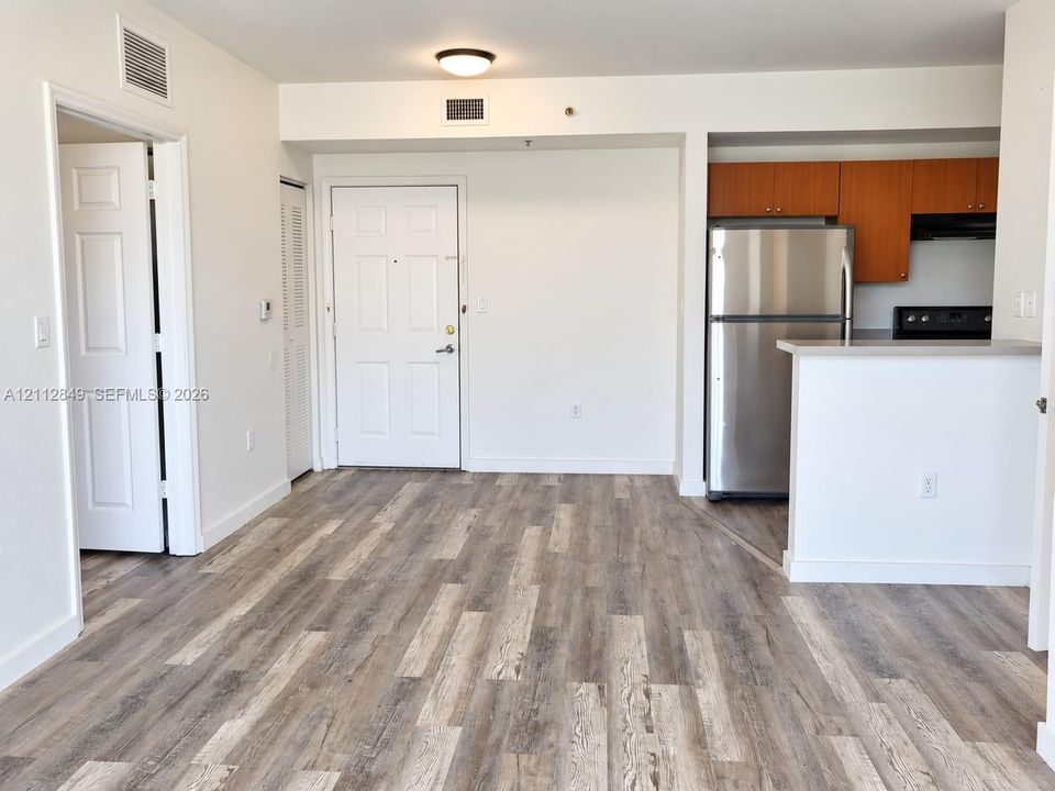 Wood-finish flooring, kitchen featuring wood-toned cabinetry, stainless steel refrigerator, and a breakfast bar