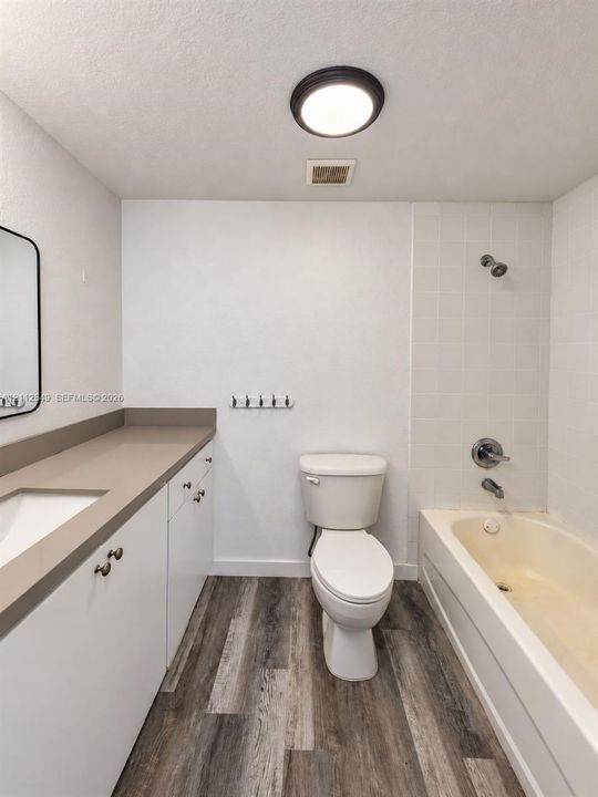 Bathroom featuring wood-finish flooring, white cabinetry with solid-surface countertops, an integrated vanity sink, and a combination tub-and-shower with wall-mounted hardware