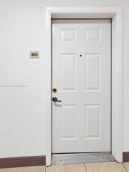 White six-panel entry door featuring a matte black lever handle, brass deadbolt, and built-in door viewer
