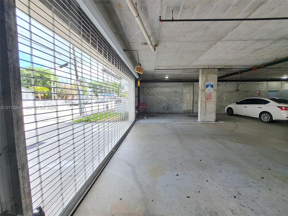Covered parking structure with concrete flooring, exposed ceiling, and integrated metal security gate