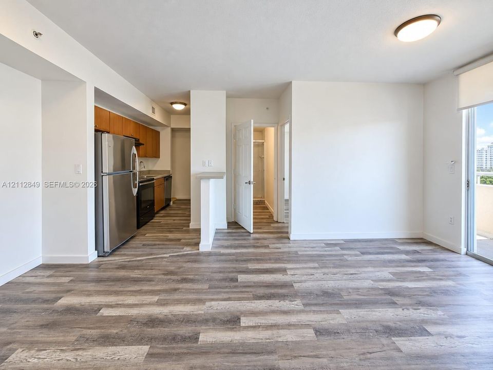 Open-concept space featuring wood-finish flooring, stainless steel kitchen appliances, wood cabinetry, and a sliding glass door leading to a balcony