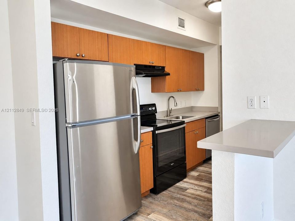 Kitchen featuring wood-finish cabinetry, stainless steel refrigerator, solid-surface countertops, wood-finish flooring, and a breakfast bar