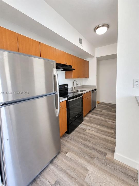 Kitchen featuring wood-finish cabinetry, stainless steel refrigerator, black electric range, and wood-finish flooring