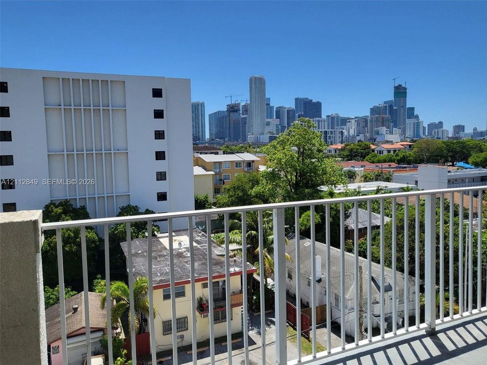 Private balcony featuring white vertical railing and concrete flooring with an urban cityscape backdrop