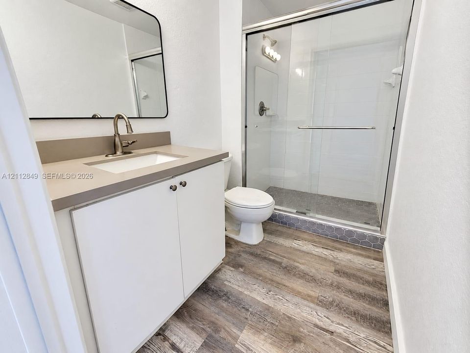 Bathroom featuring a white cabinet with a neutral-tone countertop, wood-finish flooring, and a glass-enclosed shower with tiled flooring