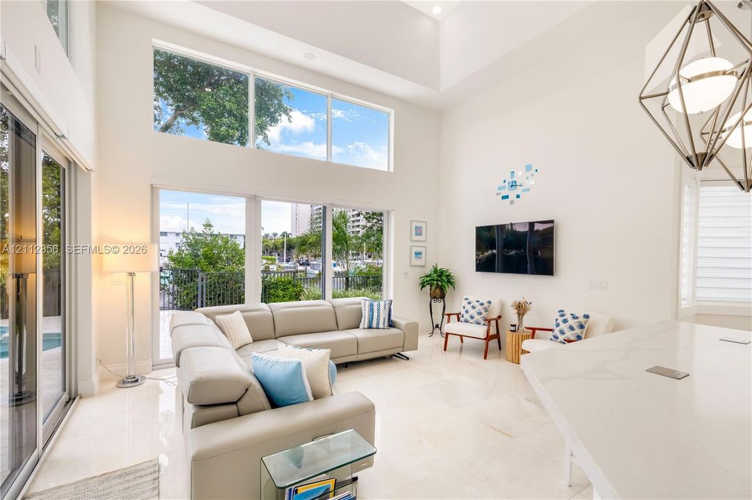 Double-height ceilings, extensive window wall, light-toned stone-finish flooring, and geometric pendant lighting