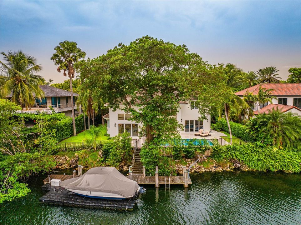 Waterfront property featuring a private boat dock, swimming pool, concrete patio, and mature trees