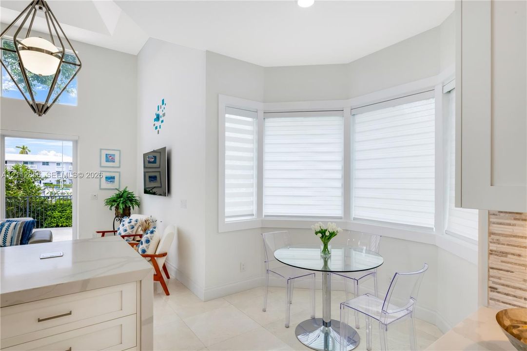 High-ceilinged room featuring a bay window, light-toned tile flooring, a geometric pendant light fixture, and a kitchen island with a stone-finish countertop