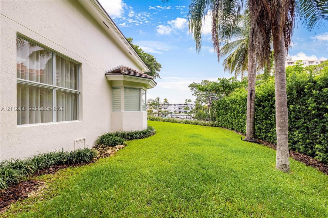 Stucco exterior featuring a bay window, expansive lawn, mature palm trees, and perimeter landscape hedging