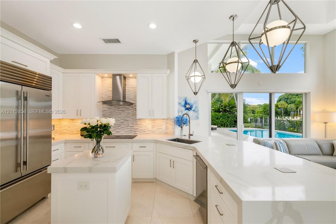Kitchen featuring white cabinetry, quartz countertops, a stainless steel refrigerator, tile backsplash, and geometric pendant lighting