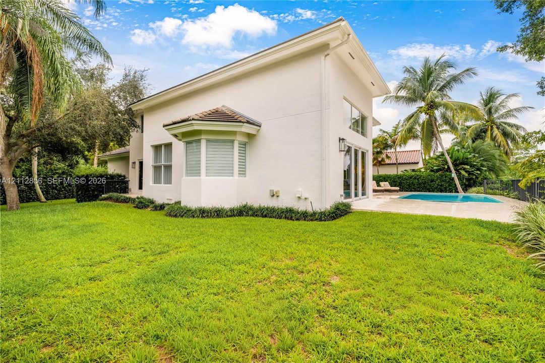 Stucco exterior featuring a bay window, expansive lawn, swimming pool with concrete decking, and floor-to-ceiling glass panel doors