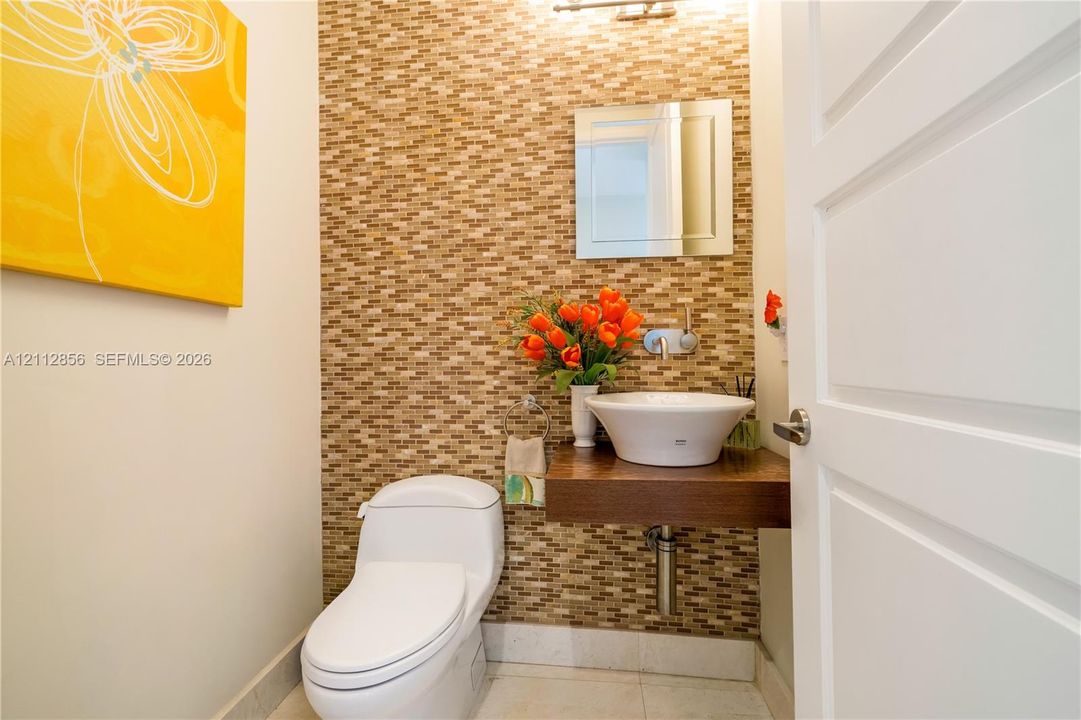 Mosaic tile wall accent, wall-mounted floating wood vanity, white vessel sink with wall-mounted faucet, and square frameless mirror