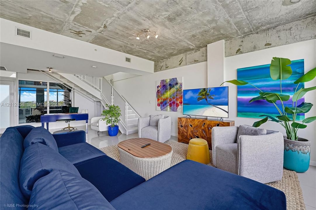 Exposed concrete ceiling, white staircase with metal railing, floor-to-ceiling glass window wall, and polished solid-surface flooring