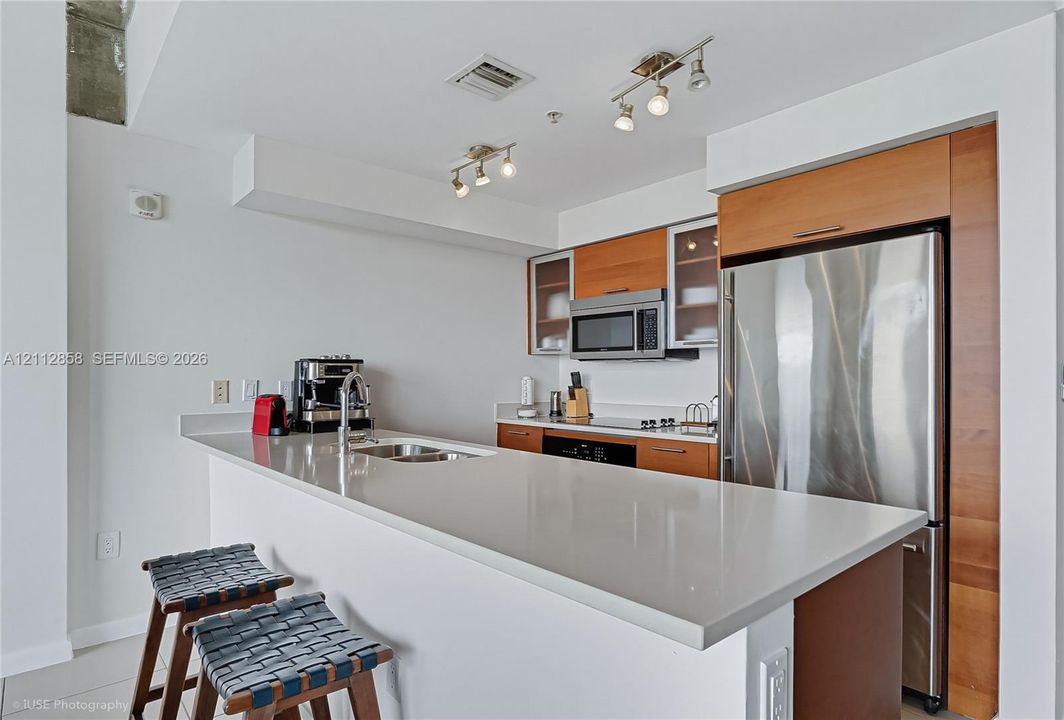 Kitchen featuring a quartz countertop, stainless steel refrigerator, microwave, and range, with wood-finish cabinetry and overhead track lighting
