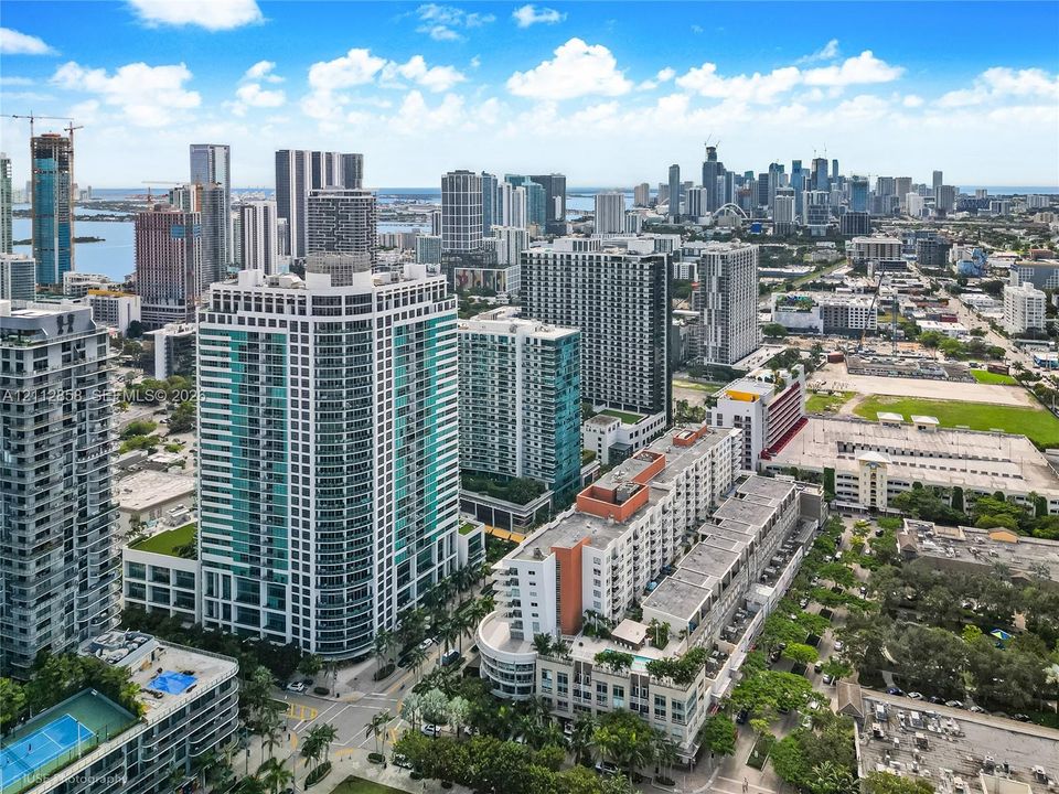 Aerial perspective of a high-rise urban environment featuring extensive glass-facade skyscrapers, multi-level parking structures, and established palm tree landscaping