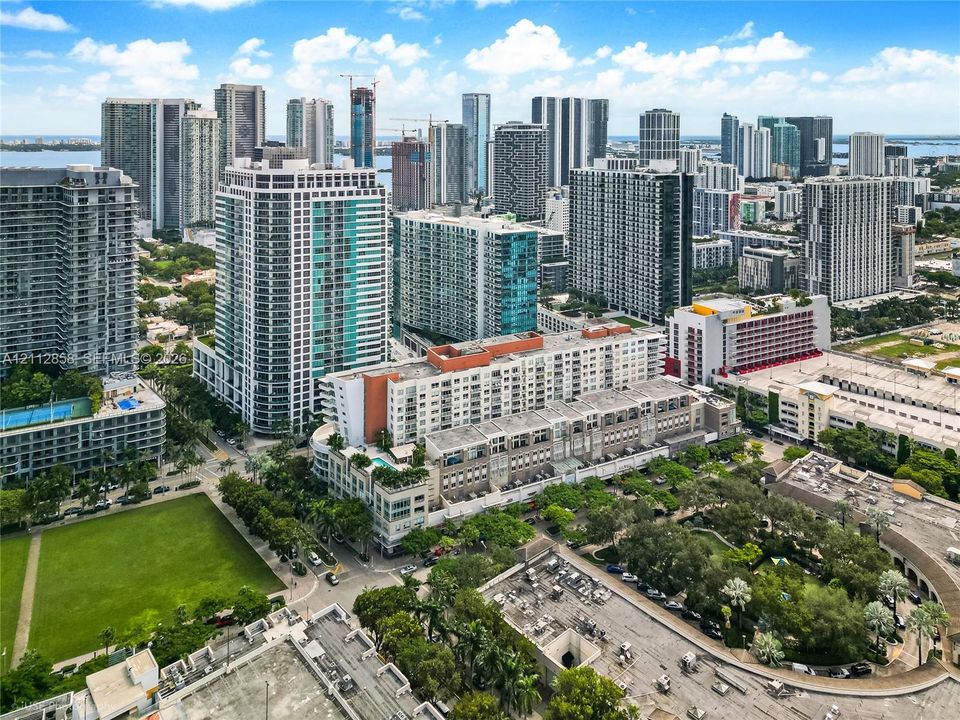 Aerial perspective featuring a mid-rise residential building with an elevated outdoor pool, expansive green space, and urban skyline backdrop