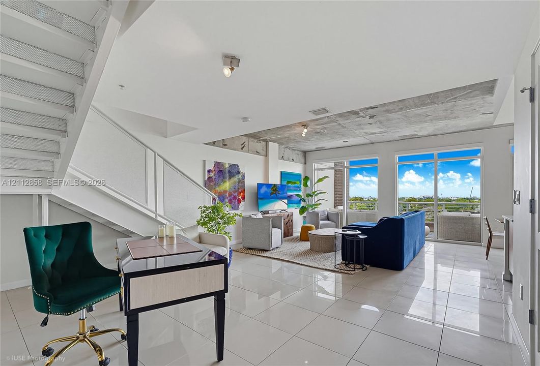 Open-concept interior featuring polished tile flooring, industrial-style exposed concrete ceiling, staircase with metal railing, and floor-to-ceiling glass panel doors