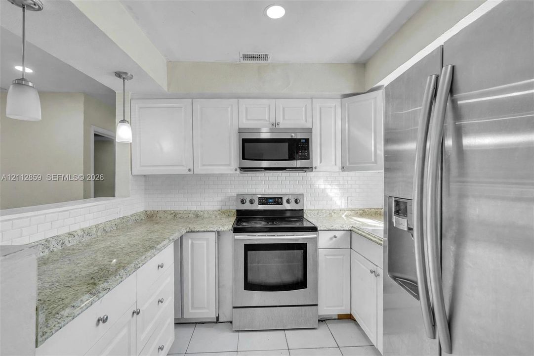 Kitchen featuring white cabinetry, stone-finish countertops, subway tile backsplash, stainless steel appliances, and pendant lighting