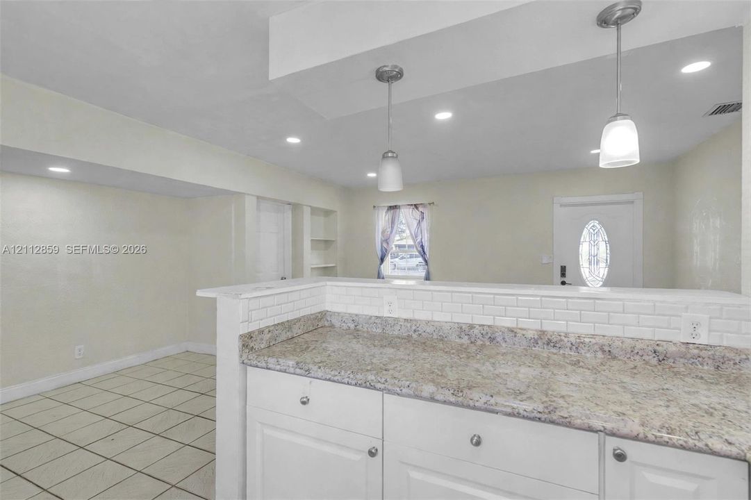 Kitchen featuring a stone-pattern countertop, white subway tile backsplash, white cabinetry, tile flooring, and dual pendant lighting