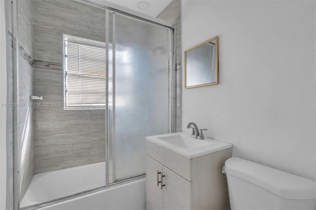 Bathroom featuring a shower-tub combination with sliding glass doors, horizontal tile wall surround, wood-finish vanity with a rectangular sink, and metallic hardware