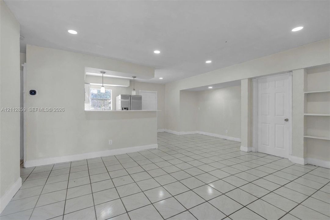 Open-concept room featuring light-colored tile flooring, recessed lighting, a kitchen pass-through counter, and built-in shelving