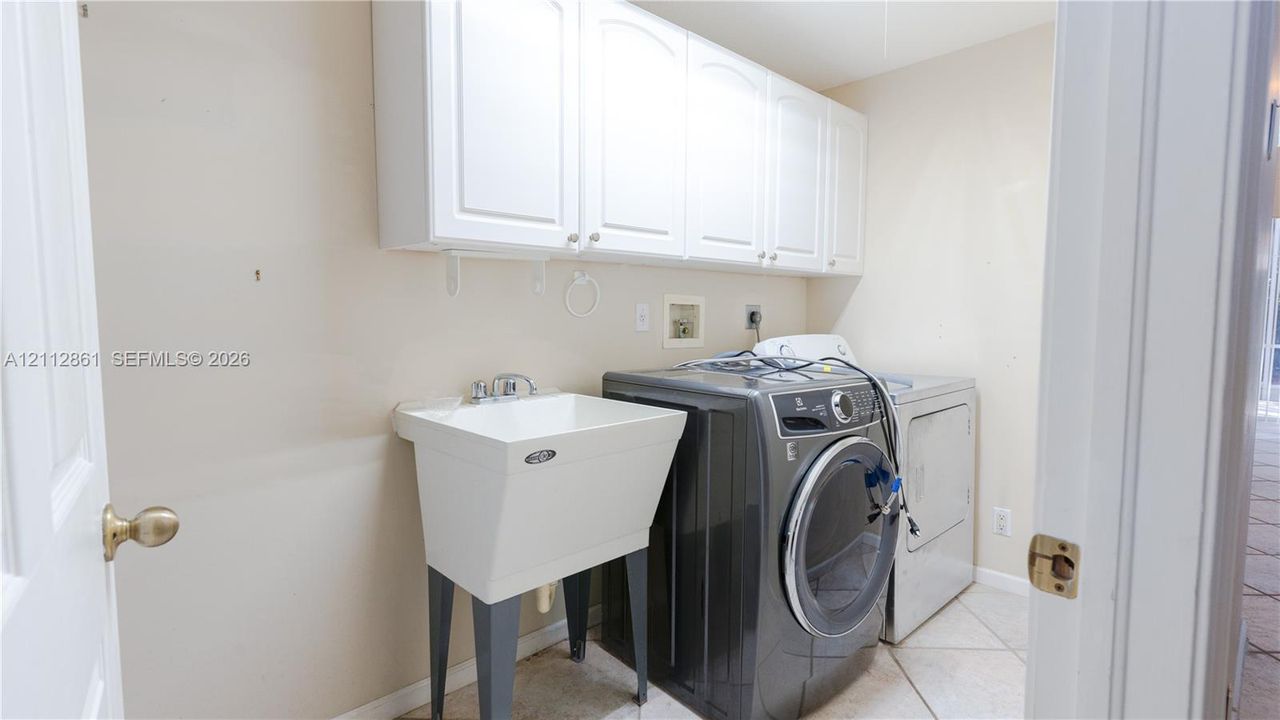 Utility space featuring white wall-mounted cabinetry, a freestanding utility sink with chrome faucet, and tiled flooring