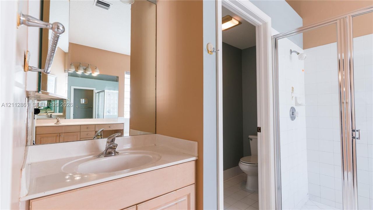 Bathroom featuring a vanity with integrated sink, expansive mirror, enclosed shower with white tile surround, and separate water closet