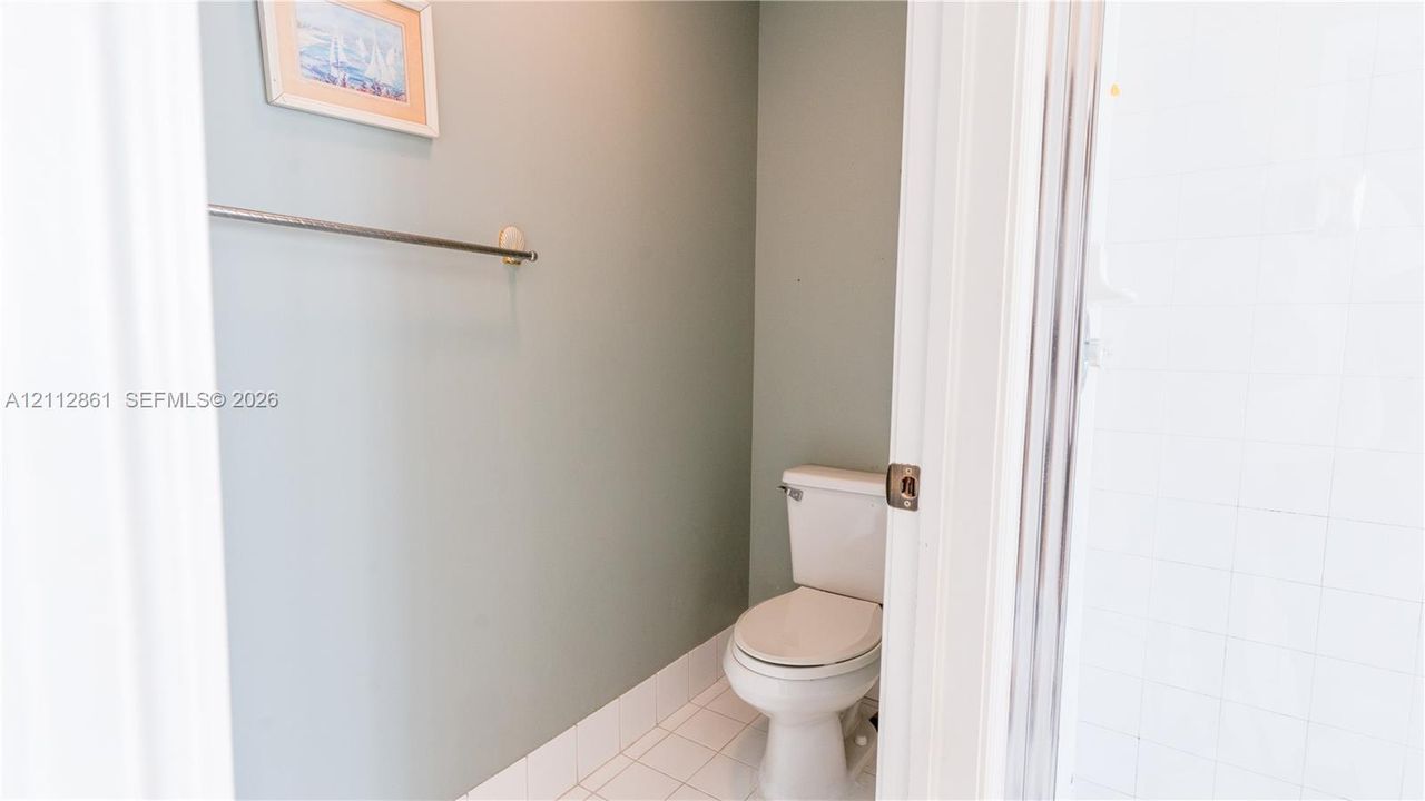 Ceramic tile flooring, white porcelain toilet, and wall-mounted metal towel bar