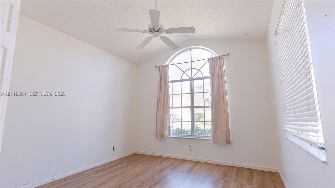 Vaulted ceiling featuring an arched window, wood-finish flooring, and a white ceiling fan