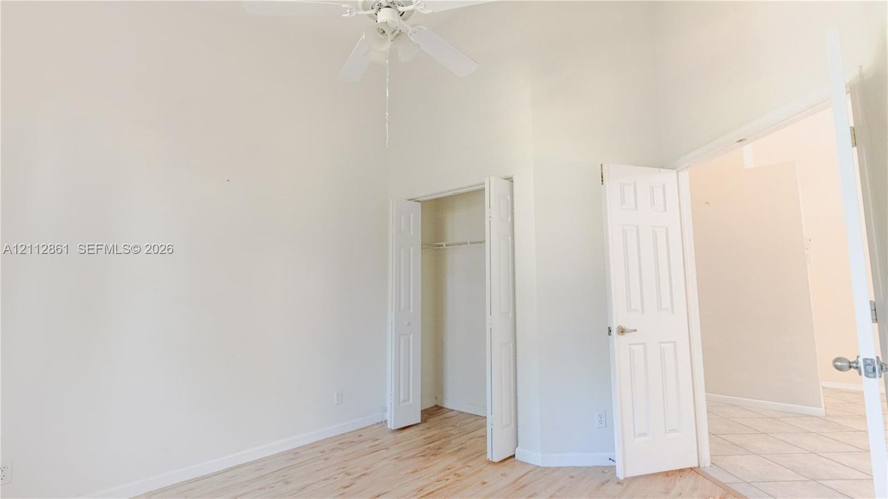 High vaulted ceiling, wood-finish flooring, white ceiling fan, and six-panel interior doors