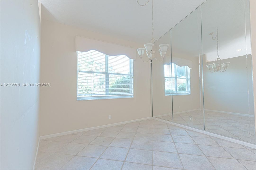 Interior room featuring large-format tile flooring, wall-to-wall mirrored closet doors, a multi-arm chandelier, and a window with custom valance