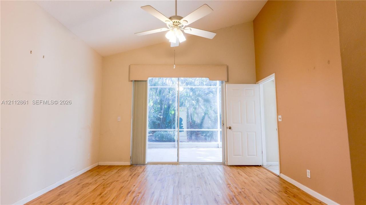 Vaulted ceiling, wood-finish flooring, ceiling fan with integrated lighting, and sliding glass doors with direct exterior access