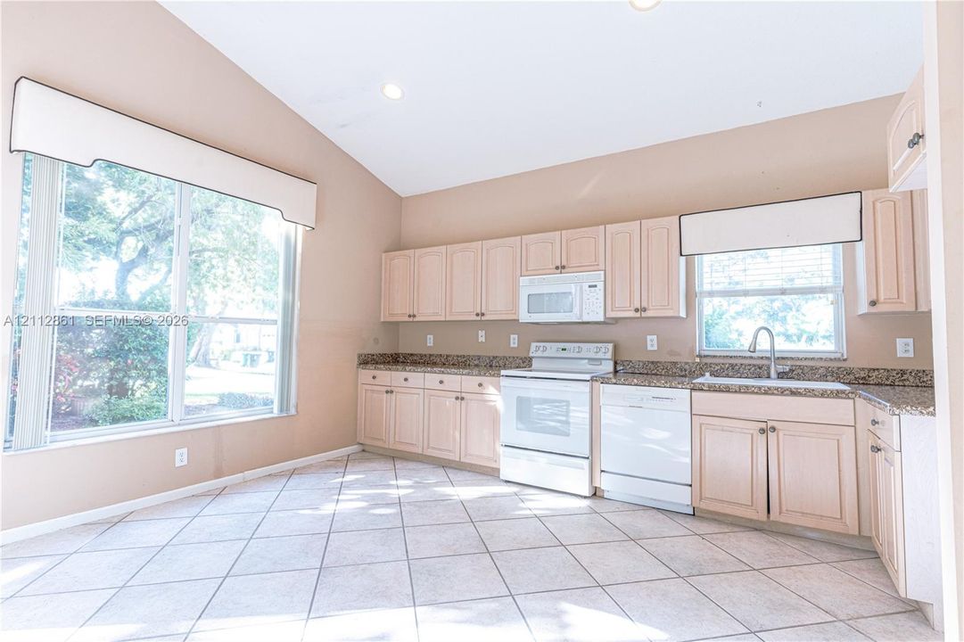 Kitchen featuring light-finish cabinetry, stone-texture countertops, tile flooring, vaulted ceilings, and large windows